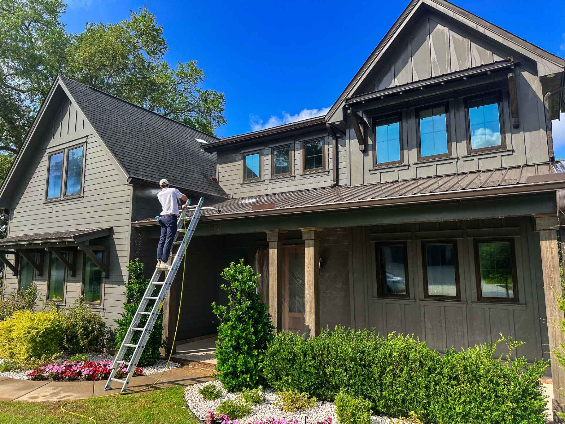 Technician soft washing a craftsman home exterior on a sunny day