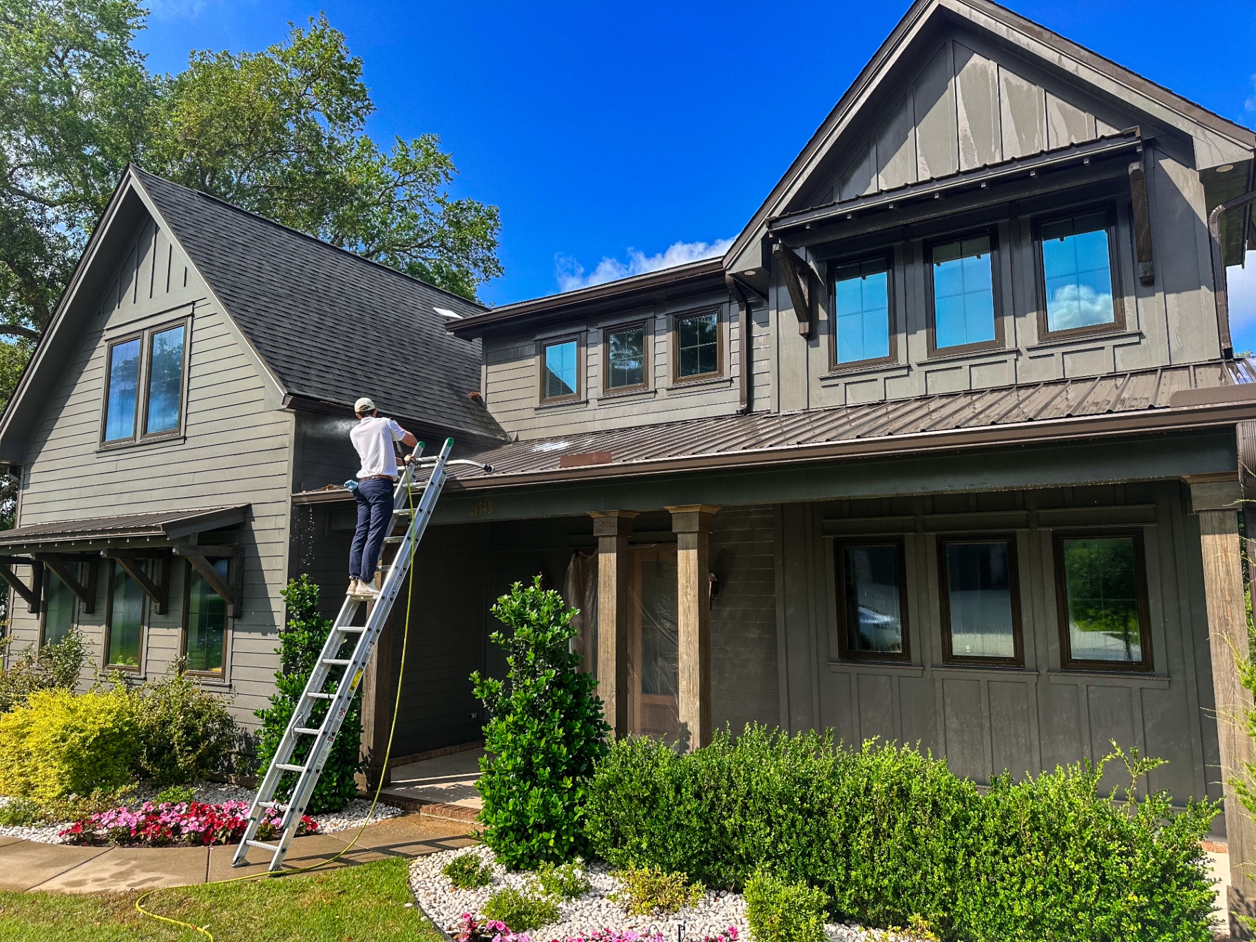 Technician soft washing a craftsman home exterior on a sunny day